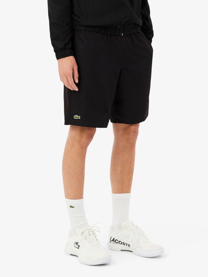 Close-up detail of LACOSTE sport shorts showing diamond taffeta texture and green crocodile embroidery