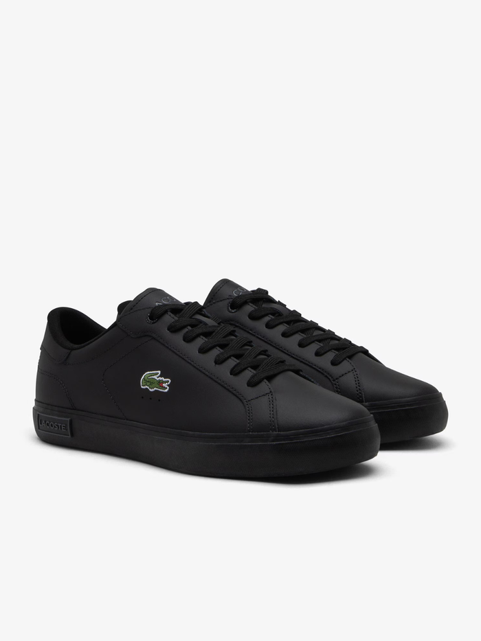 Close-up of LACOSTE Powercourt black leather sneaker heel with embossed LACOSTE text branding and white midsole detail