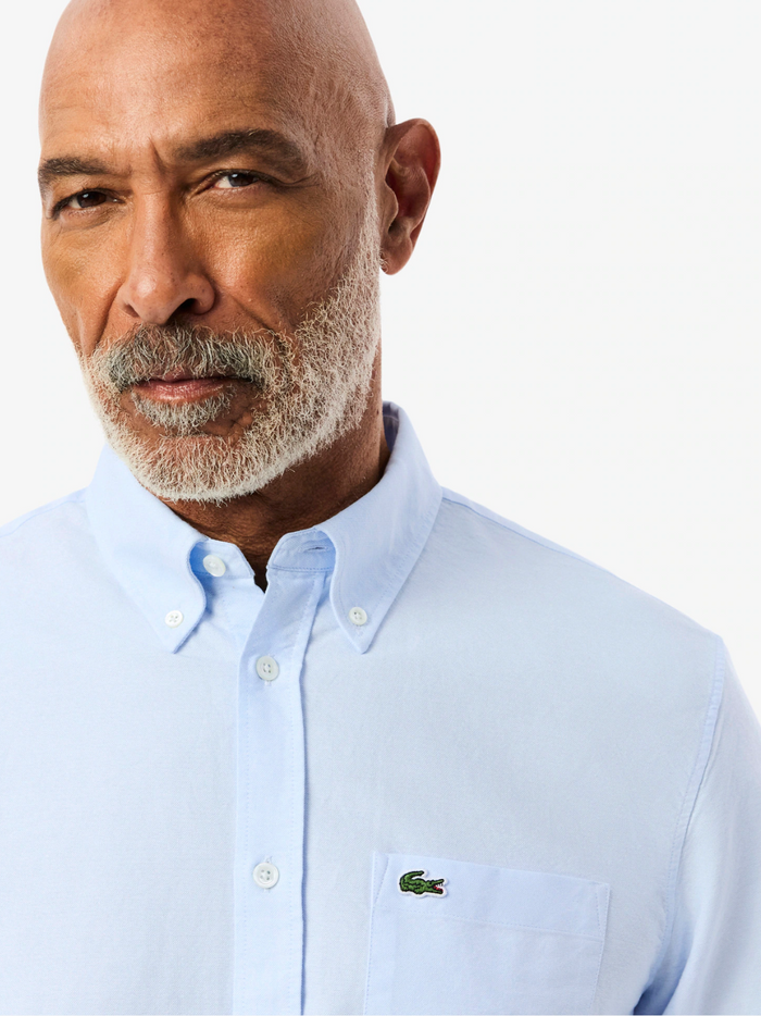 Close-up detail of LACOSTE Regular Fit Oxford Shirt showing light blue Oxford weave texture, button quality and fine craftsmanship