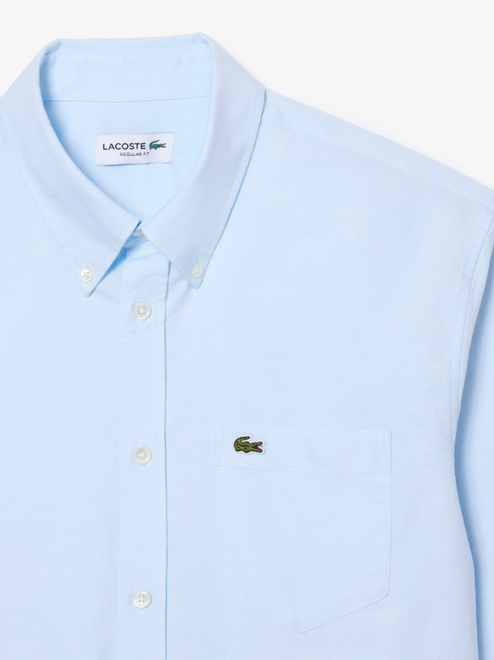 LACOSTE Regular Fit Oxford Shirt collar and chest detail featuring the iconic LACOSTE crocodile logo on light blue Oxford cotton