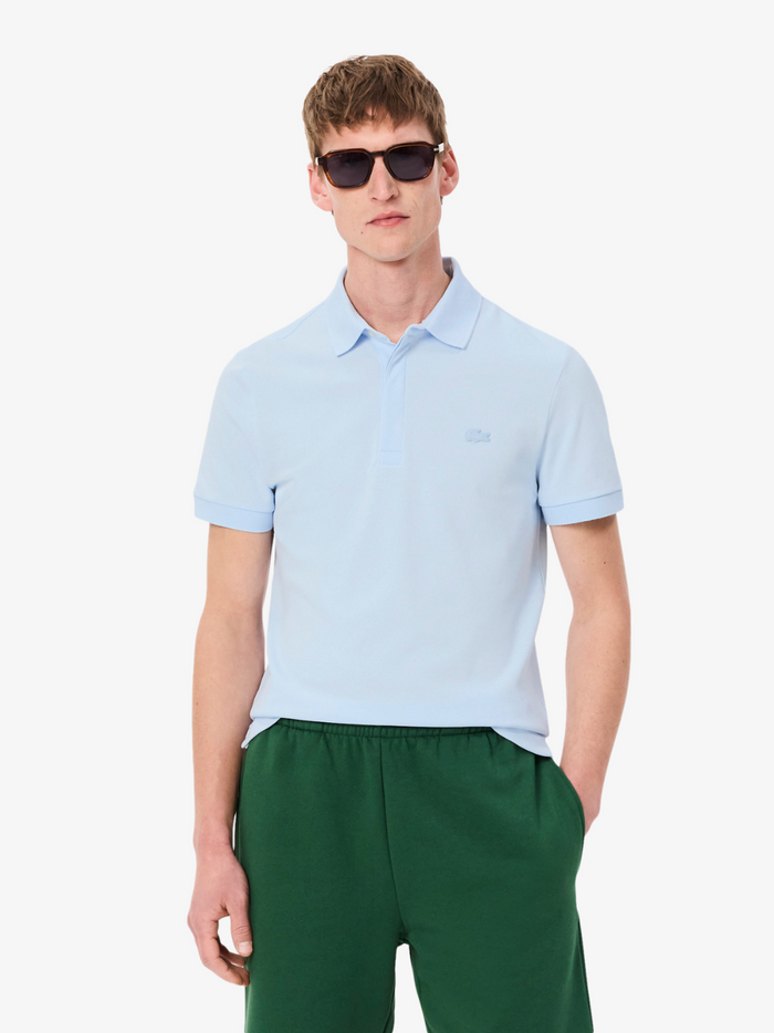 Man wearing a light blue polo shirt and green pants on a white background