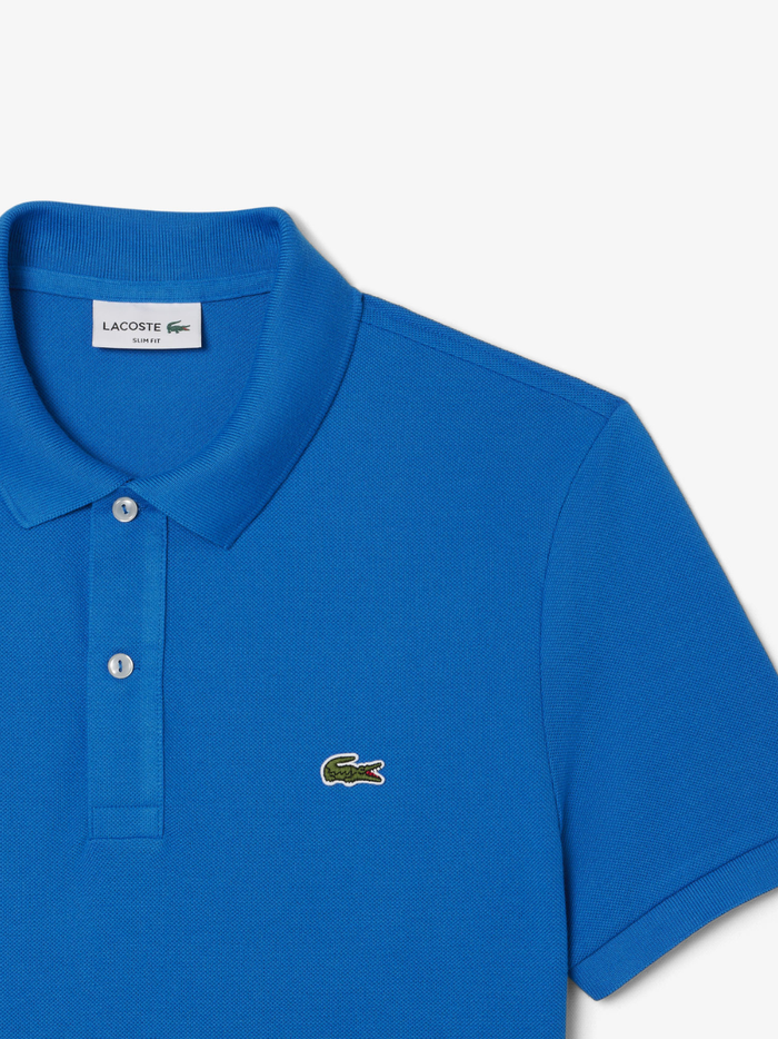 Detail shot of iconic LACOSTE green crocodile embroidery on denim blue L.12.12 piqué polo shirt chest