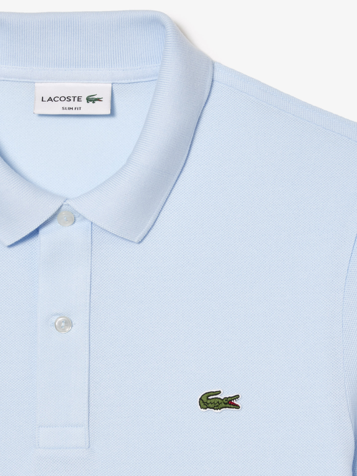 Detail shot of iconic LACOSTE green crocodile embroidery on light blue L.12.12 piqué polo shirt chest