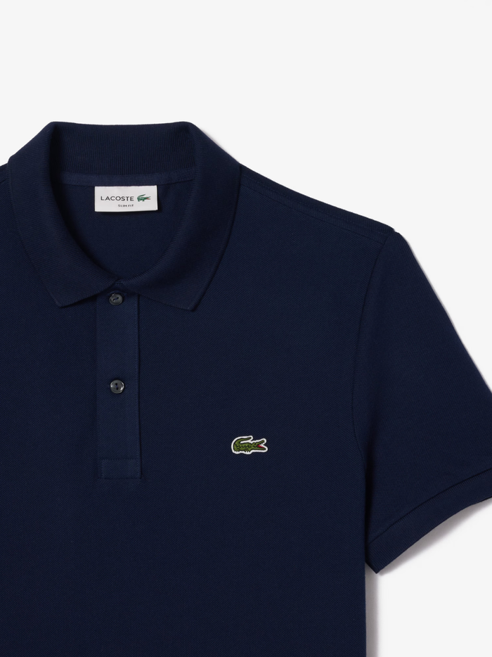 Detail shot of iconic LACOSTE green crocodile embroidery on midnight blue L.12.12 piqué polo shirt chest