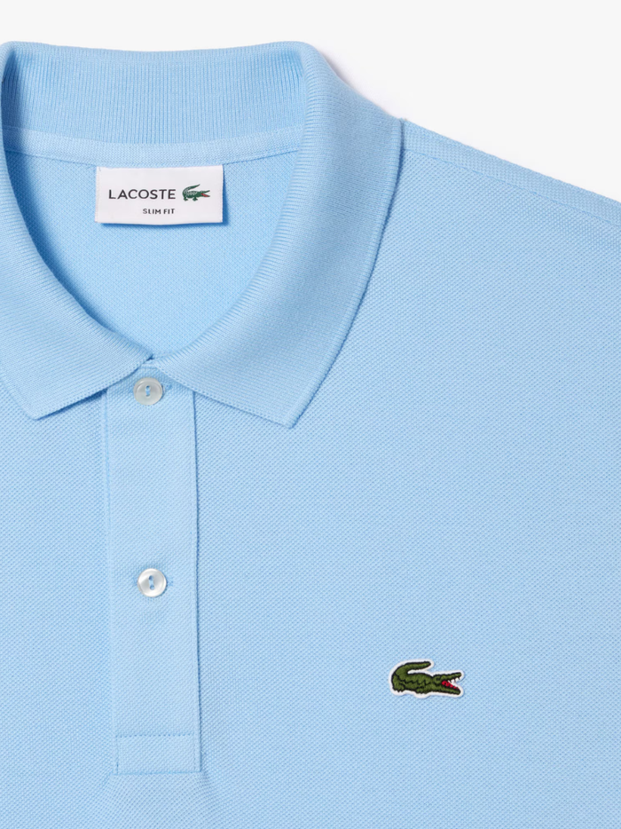 Detail shot of iconic LACOSTE green crocodile embroidery on pale blue L.12.12 piqué polo shirt chest