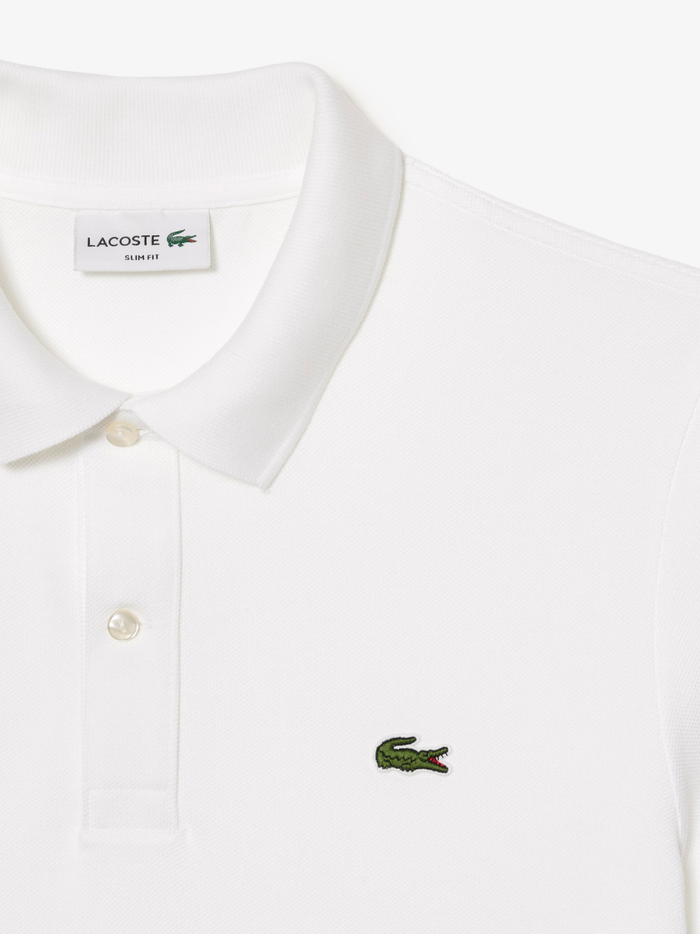 Detail shot of iconic LACOSTE green crocodile embroidery on white L.12.12 piqué polo shirt chest