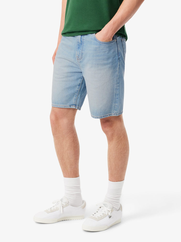 Close-up detail of LACOSTE Bermuda shorts showing light wash canvas and green pocket seams